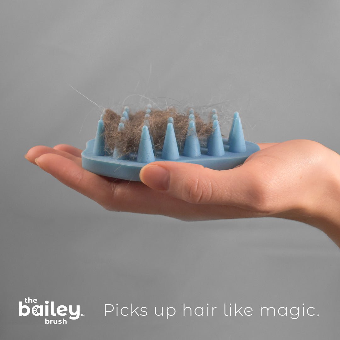 A beautiful womans hand holds the blue bailey brush in her open palm showing off a large clump of cat hair within it.